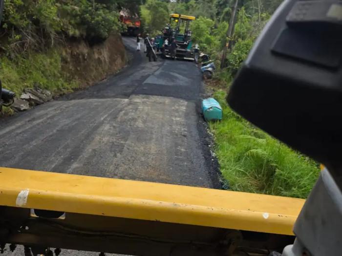 Proceso de compactado y nivelación de capa asfáltica en camino rural visto desde maquinaria pesada.