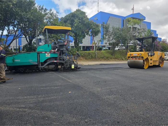 Pavimentación y compactación de asfalto en zona urbana mediante pavimentadora Vögele y rodillo CAT.