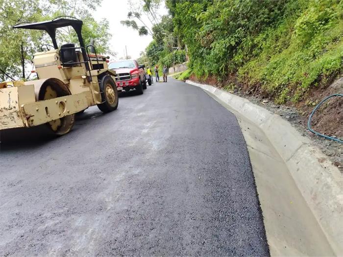 Compactación final de carpeta asfáltica y cunetas de concreto en carretera de montaña.