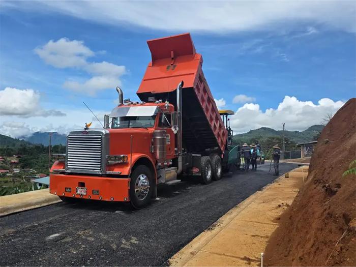Camión de volteo alimentando asfalto a la pavimentadora durante la construcción de una calle.