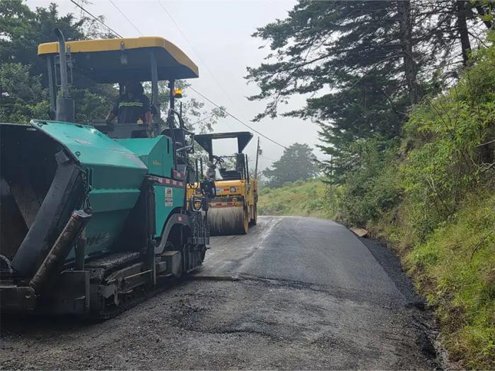 Maquinaria de asfaltado y rodillo compactador trabajando en la pavimentación de un camino de montaña