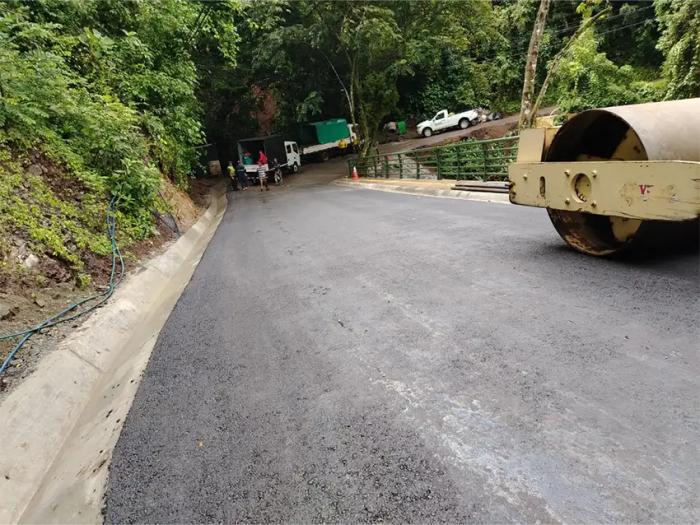 Compactación de carpeta asfáltica recién colocada en vía con cuneta de concreto y rodillo en pendien
