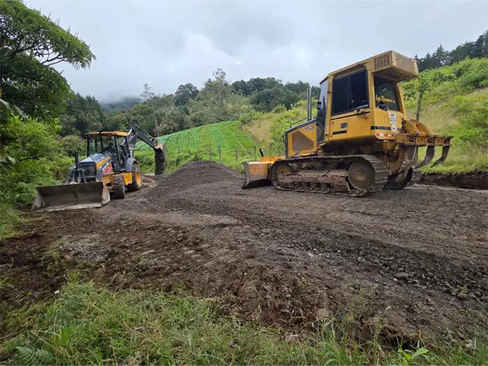 Tractor de orugas y retroexcavadora realizando extendido de material granular y nivelación de camino